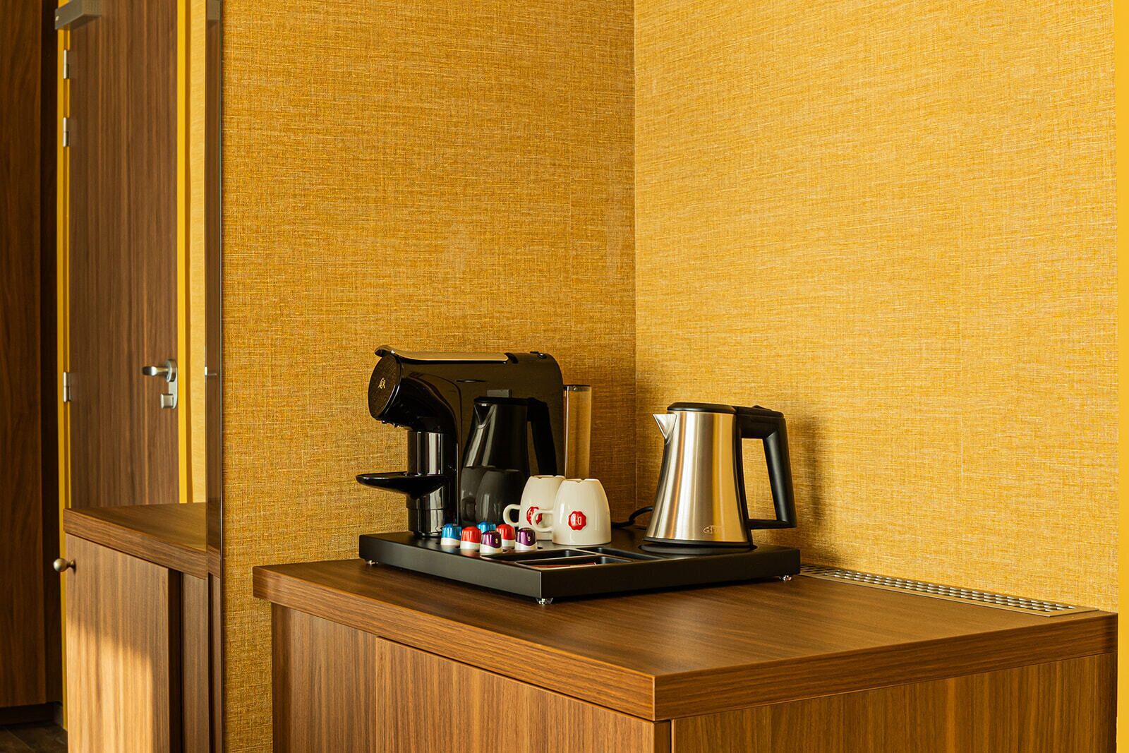 Una kitchenette compacta con cafetera, hervidor y algunas tazas sobre una encimera de madera.