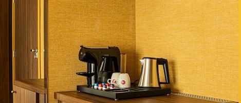 Una kitchenette compacta con cafetera, hervidor y algunas tazas sobre una encimera de madera.