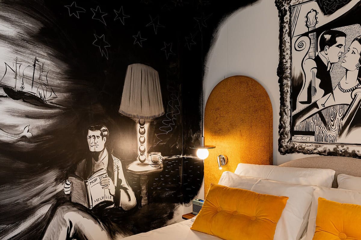 A room with a bed, a lamp, a wall mural, and a framed picture.