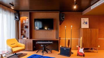 Una sala de estar moderna con un televisor de pantalla plana grande, un teclado, un otoman azul, un sillón amarillo y una guitarra.