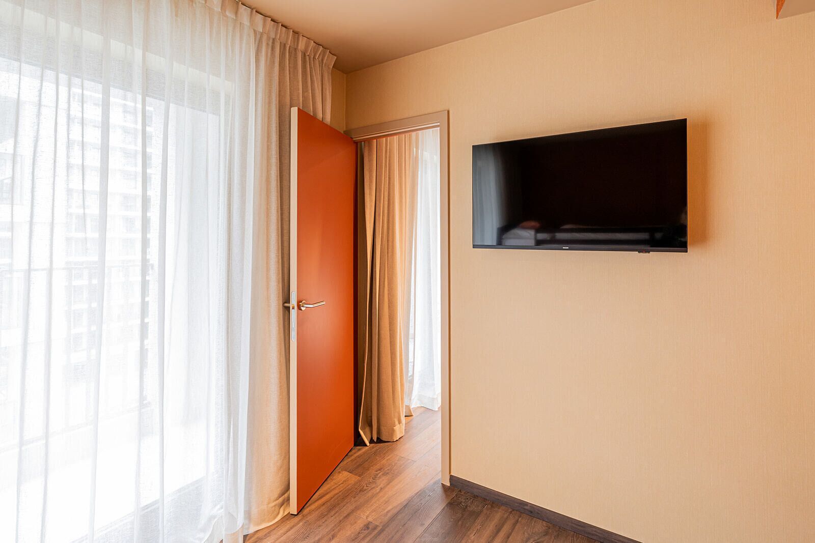 A hallway with a wooden floor, a door with a handle, and a wall-mounted television.