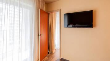 A hallway with a wooden floor, a door with a handle, and a wall-mounted television.