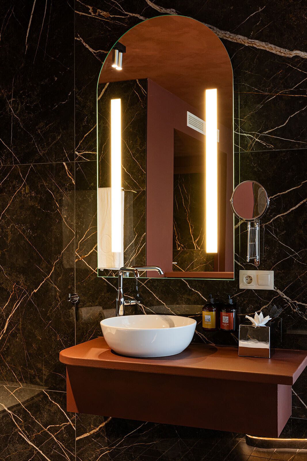 Un baño con salpicadero de mármol, un lavabo blanco e iluminación integrada en un espejo.