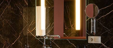 Un baño con salpicadero de mármol, un lavabo blanco e iluminación integrada en un espejo.