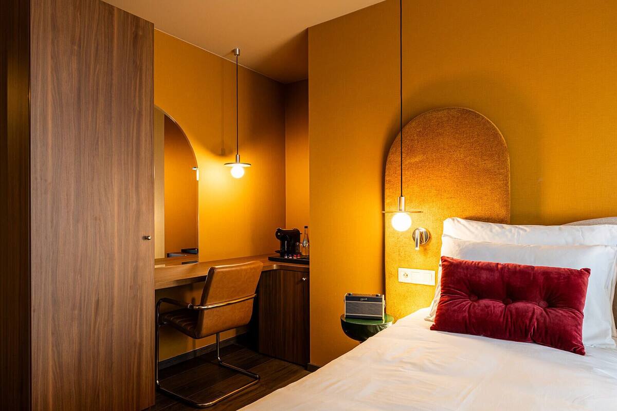 A hotel room with a bed, a desk with a chair, a coffee machine, and a lamp.