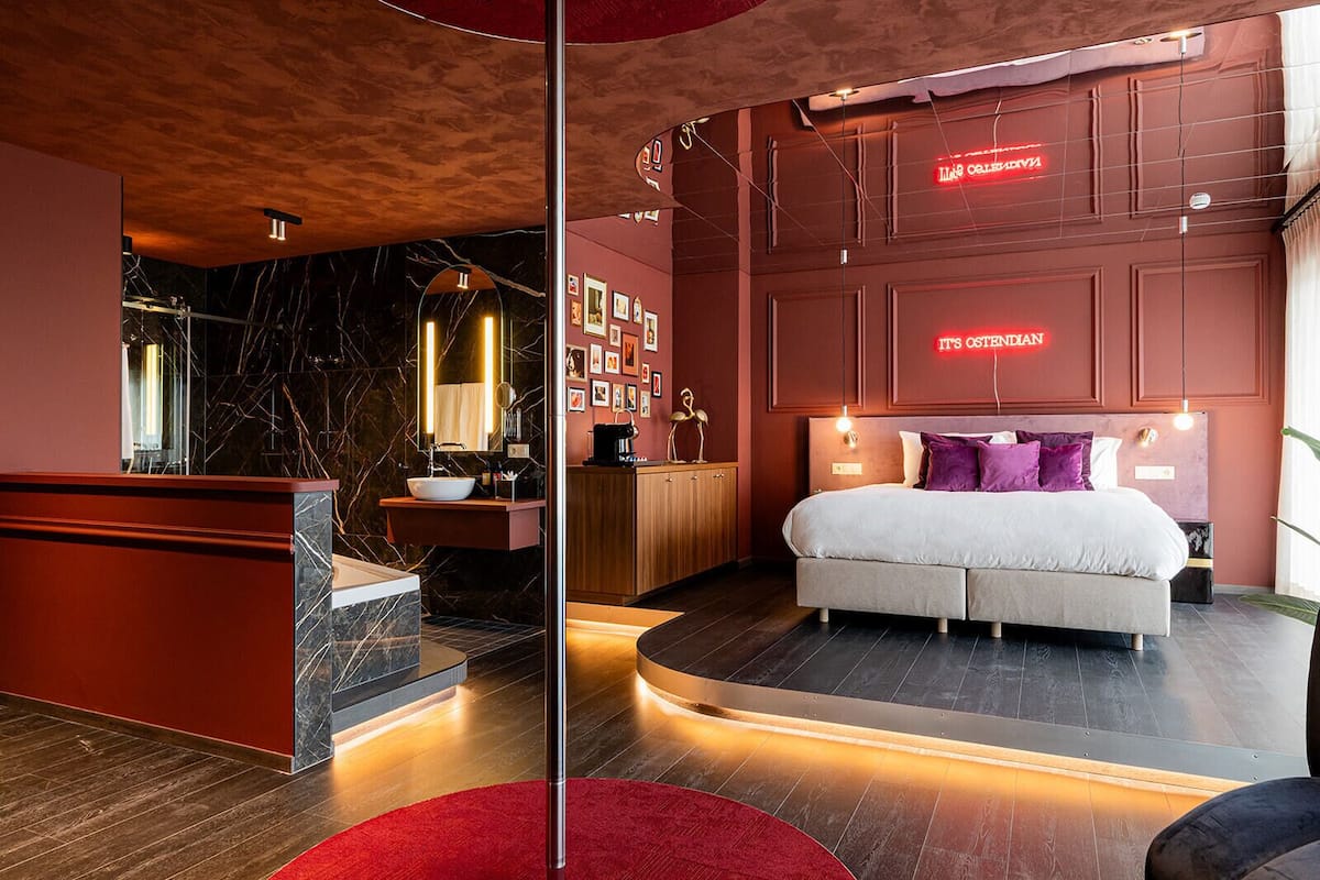 A modern bedroom with a large bed, a vanity with a mirror, and a red accent wall.
