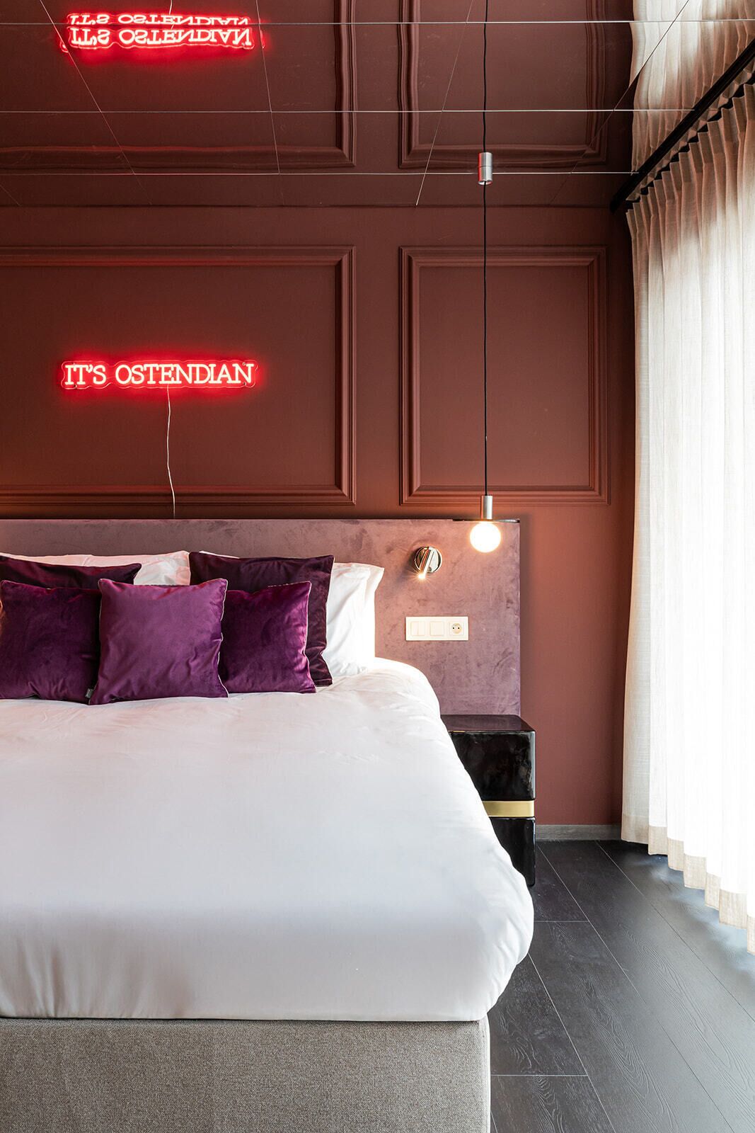 A modern hotel room with a large bed, a headboard with a light fixture, and a neon sign on the wall.