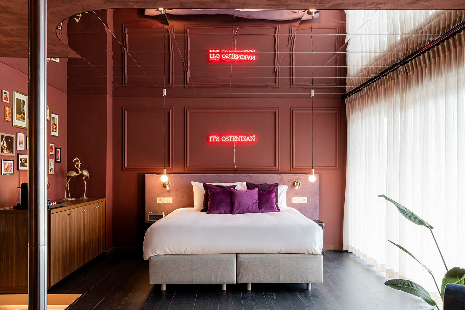 Een moderne slaapkamer met een groot bed, twee nachtkastjes, een houten dressoir en een neonbord aan de muur.