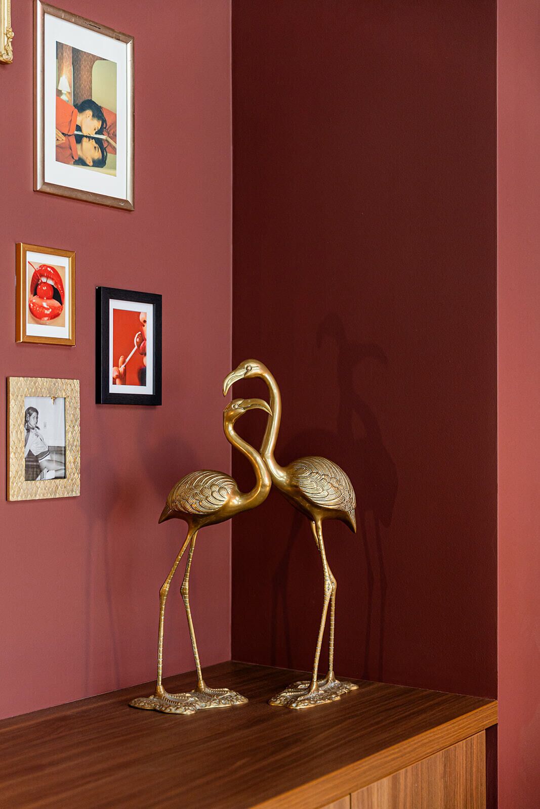 Una habitación con una mesa de madera que muestra dos esculturas doradas de cisnes, una pared roja y varias fotografías enmarcadas.