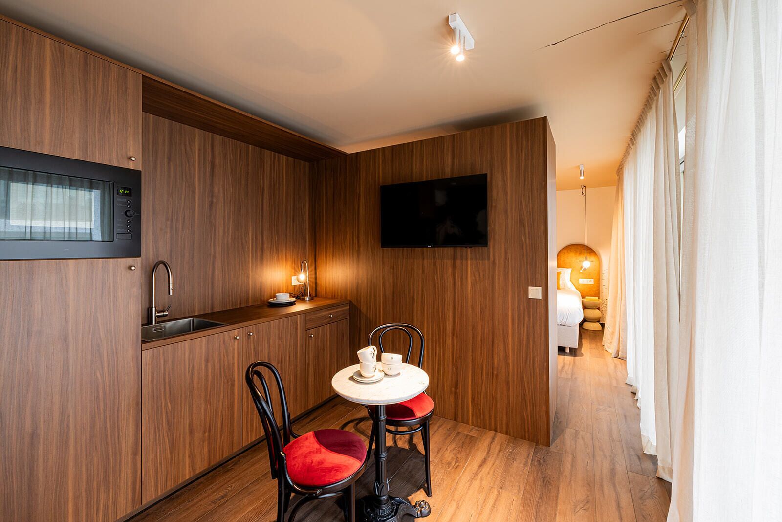 Cocina compacta con muebles de madera, microondas, pileta y un comedor con dos sillas y una mesita.