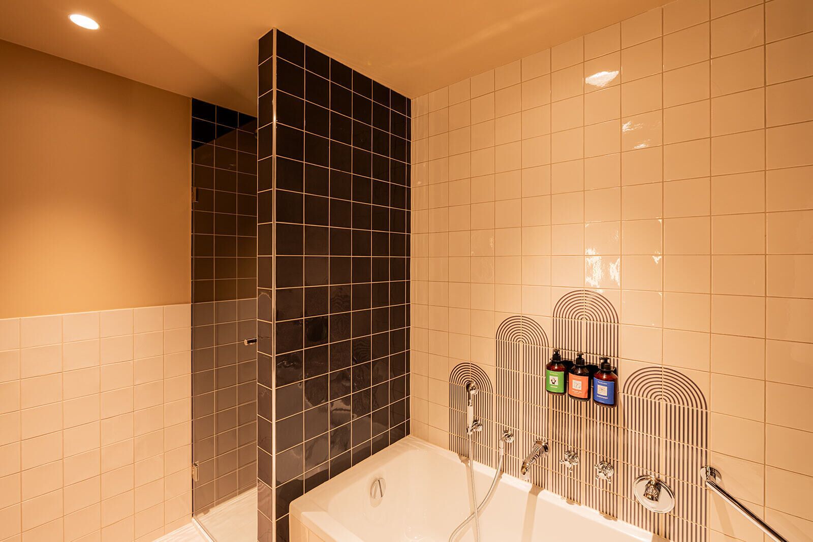 A modern bathroom with a bathtub, a shower area, and a tiled wall with a unique pattern.