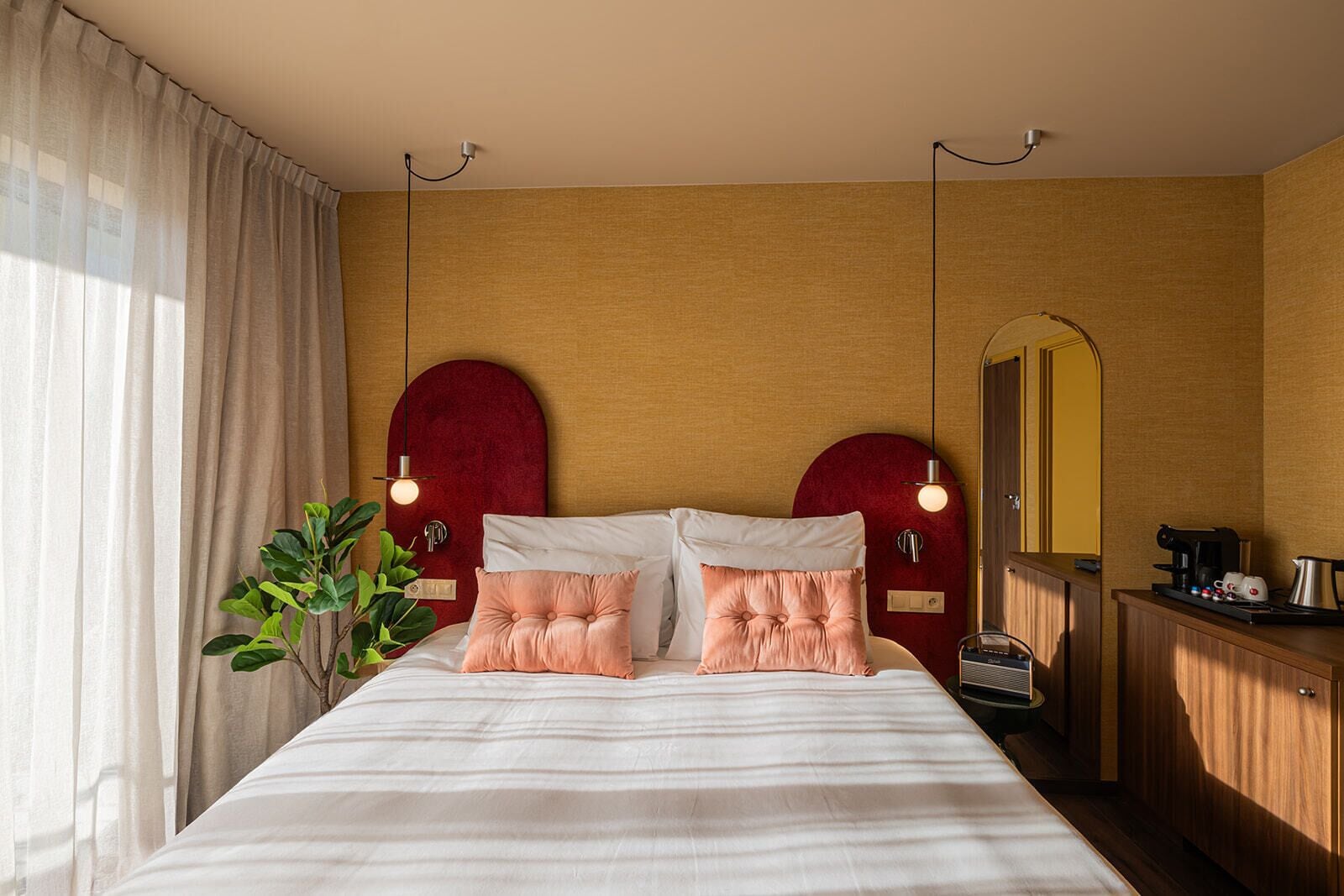 Camera d'albergo con un letto grande, due testiere rosse, un comodino con una radio e uno specchio.