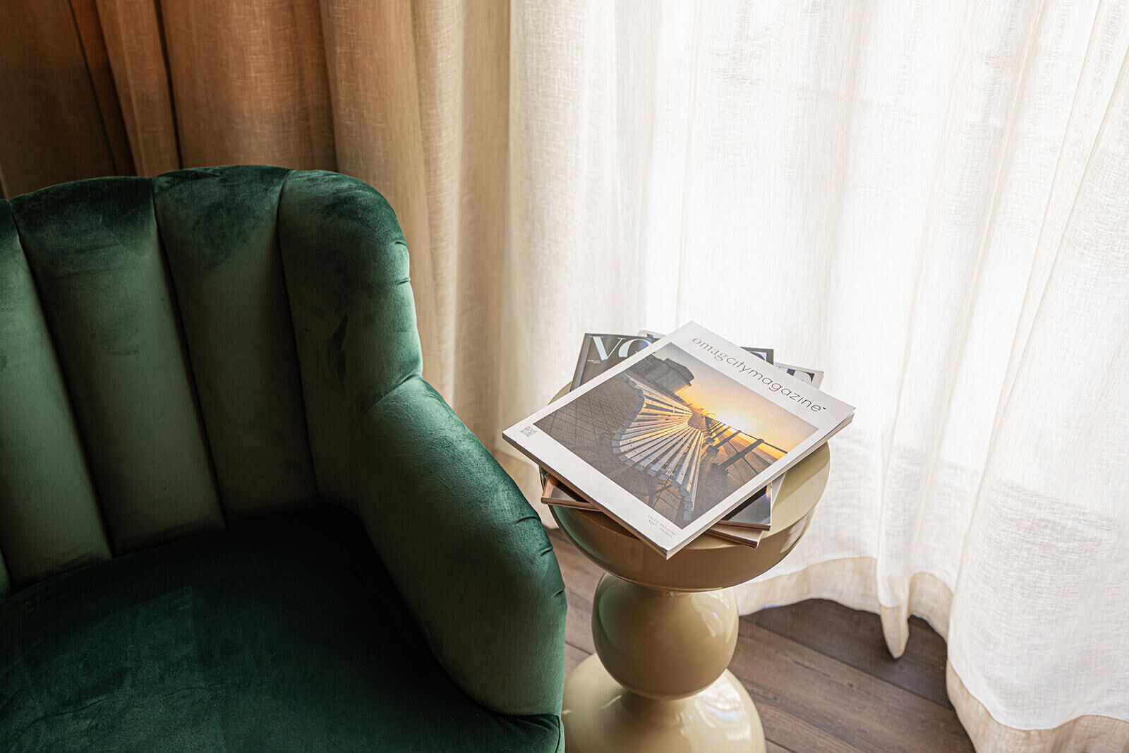 A green armchair next to a small table with a magazine on it.