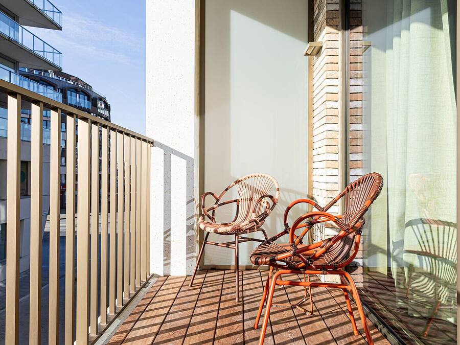 A balcony with two wicker chairs, a metal railing, and a view of a building in the background.