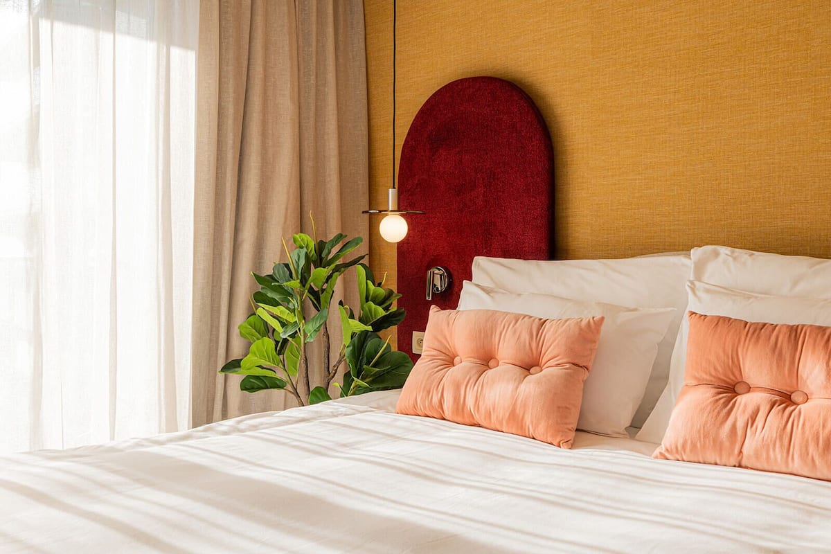 A neatly made bed with two pink pillows, a red headboard, and a bedside lamp.