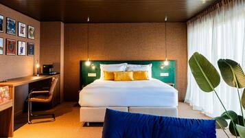 A modern hotel room with a large bed, a desk with a coffee machine, and a chair.