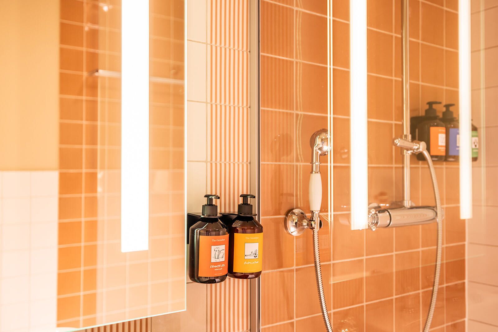 A bathroom with orange tiles, a shower, and two bottles of shampoo.