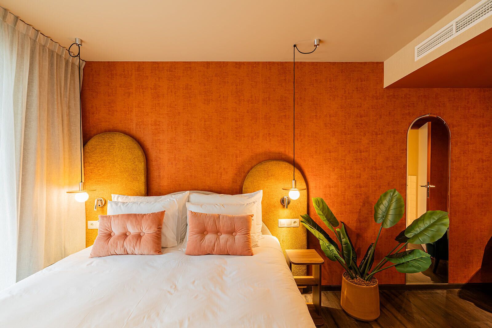 A hotel room with a large bed, two bedside tables, a potted plant, and a mirror on the wall.