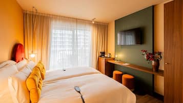 A hotel room with two beds, a desk with a chair, a television, and a window with curtains.