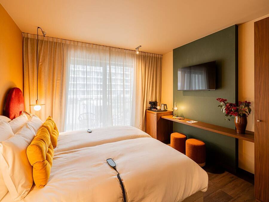 A hotel room with two beds, a desk with a chair, a television, and a window with curtains.
