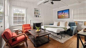 Een knus ingerichte kamer met een bed, een bank, een stoel, een salontafel, een open haard en een plafondventilator.