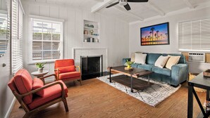 Een ruime woonkamer met een open haard, een plafondventilator en een groot raam met luxaflex.