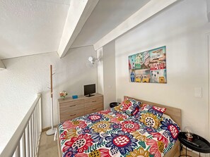 Cozy loft-style room with a central bed, bedside table, and mounted TV.