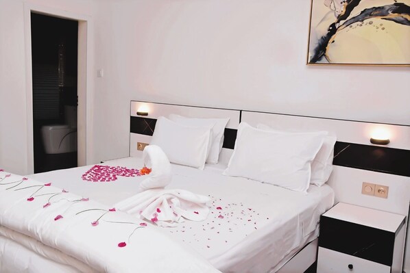 A neatly made bed with white linens and pink flower petals, a wall-mounted light, and a painting above the bed. - Keur Adiana (Mbour)