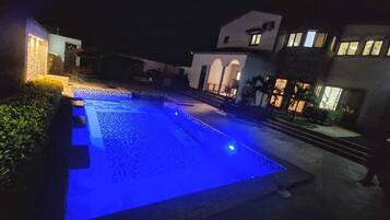 A swimming pool with blue lighting at night, surrounded by buildings with illuminated windows.