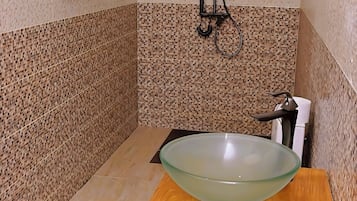 Baño con lavamanos de vidrio, ducha de mano y toallero.