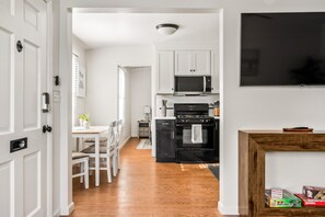 A modern kitchen with white cabinets, a black stove, and a microwave. There is a dining area with a table and chairs. - Beautiful Windansea Beach Compound Steps to Sand (San Diego)