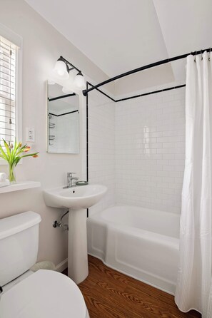 Un bagno con lavandino bianco, specchio e servizi igienici, una doccia con tenda nera e pavimento in legno.