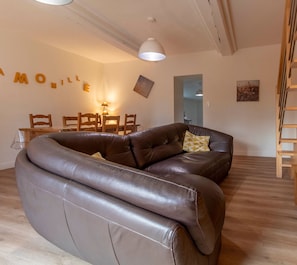 A modern living room with a brown leather sofa, wooden dining table, and chairs.