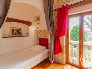 Ein Schlafzimmer mit einem Einzelbett, einem Fenster mit roten Vorhängen, einer Holzbalkendecke und einer Steinwand.