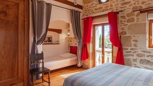 A bedroom with a wooden bed, a bench, and a view of the outdoors through a window with red curtains. - Charming retreat in Saint-Georges near Doué-en-Anjou (Doué-en-Anjou)