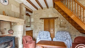 A rustic room with a stone wall, wooden staircase, a fireplace, and two patterned armchairs. - Charming retreat in Saint-Georges near Doué-en-Anjou (Doué-en-Anjou)