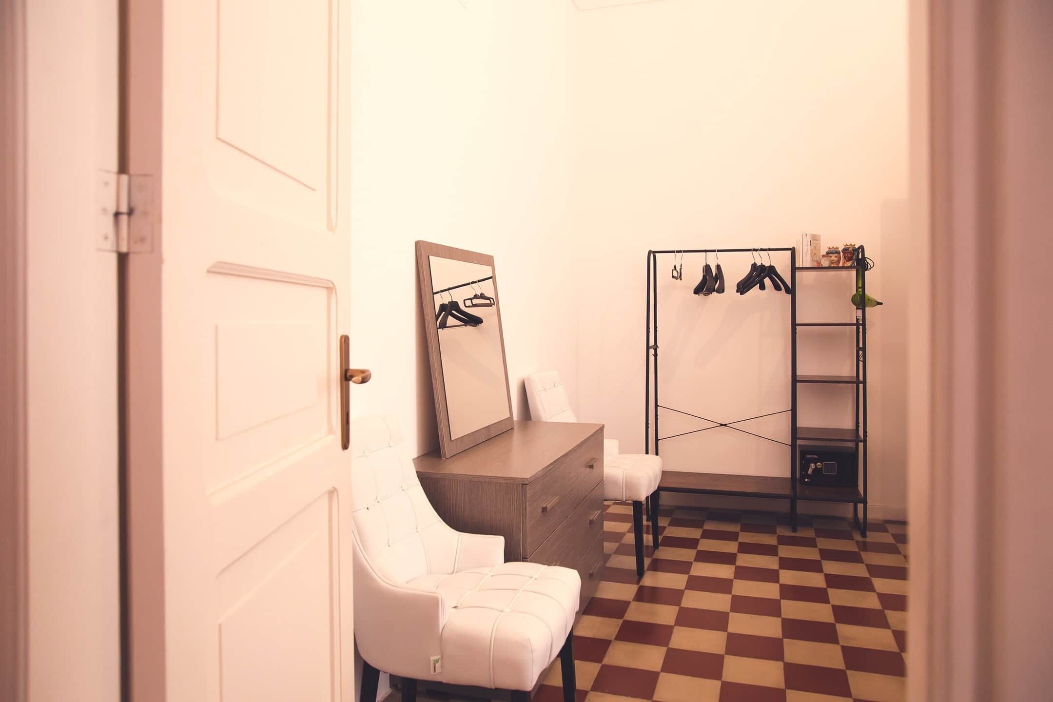 A room with a checkered floor, a white chair, a dresser, a mirror, and a shoe rack.