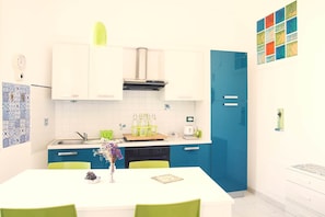 A modern kitchen with white cabinets, a blue door, and a dining table with chairs. - Alive – Spacious Seaview Apartment in Balestrate (Balestrate)