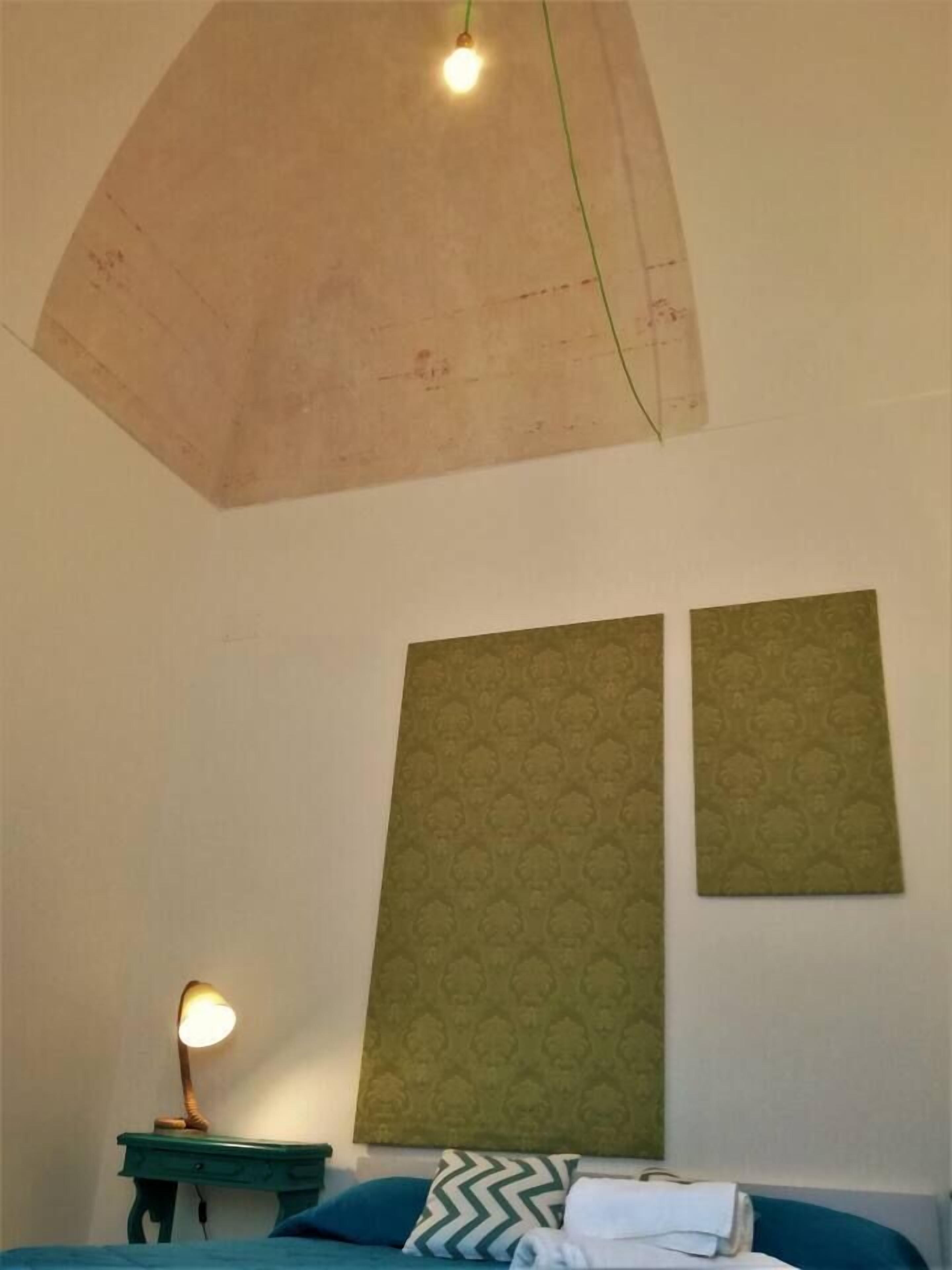 A room with a bed, a nightstand with a lamp, and two patterned wall hangings.