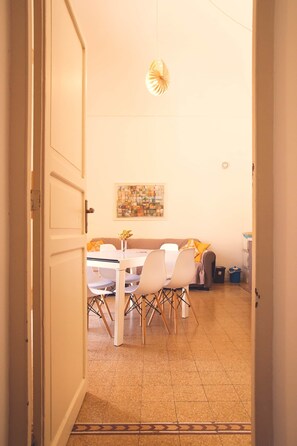 Une porte ouverte donne sur un espace repas comprenant une table et des chaises, un luminaire suspendu et une œuvre d’art accrochée au mur.