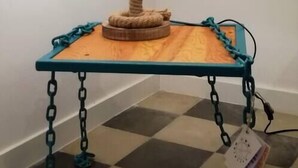 Luminária com base de corda sobre mesa de madeira com pés azuis-esverdeados e correntes.