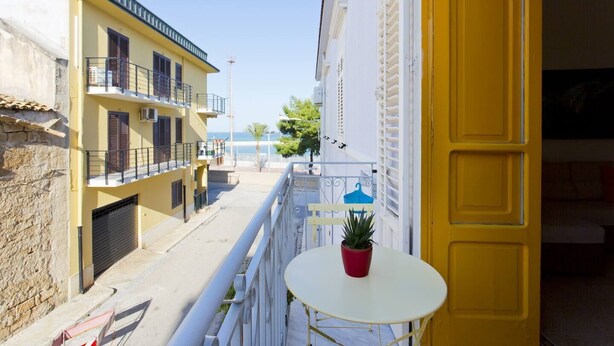 Uma rua estreita com edifícios amarelos, uma varanda com planta em vaso e vista para o mar.