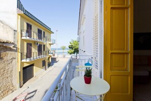En smal gade med gule bygninger, en balkon med en plantekasse, og udsigt til havet.