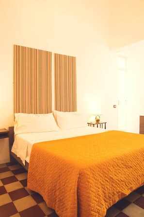 Une chambre d’hôtel avec un lit, une table de chevet, une lampe et un sol à carreaux.