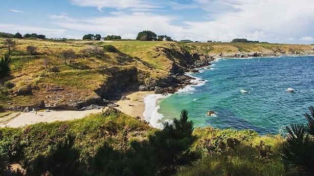 Paisaje costero con una playa, acantilados rocosos y un cielo despejado.