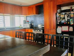 Kitchen with gas stove, microwave, and refrigerator, featuring a tiled backsplash and window.