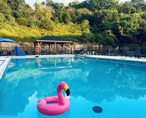 A swimming pool with a pink flamingo float, a covered seating area, and a fence. - Branson Breeze: 4BR Family Retreat with Arcade & 5★ Location, Double Living Room (Branson)