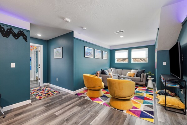 Un salon moderne aux murs de couleur turquoise, avec un canapé gris, des fauteuils jaunes et un tapis aux couleurs vives.