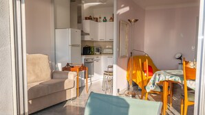 Un espacio habitable compacto con sofá, mesa de comedor, sillas, zona de cocina y un balcón con fruta.