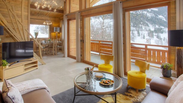 A cozy living room with a television, sofa, coffee table, and yellow chairs.